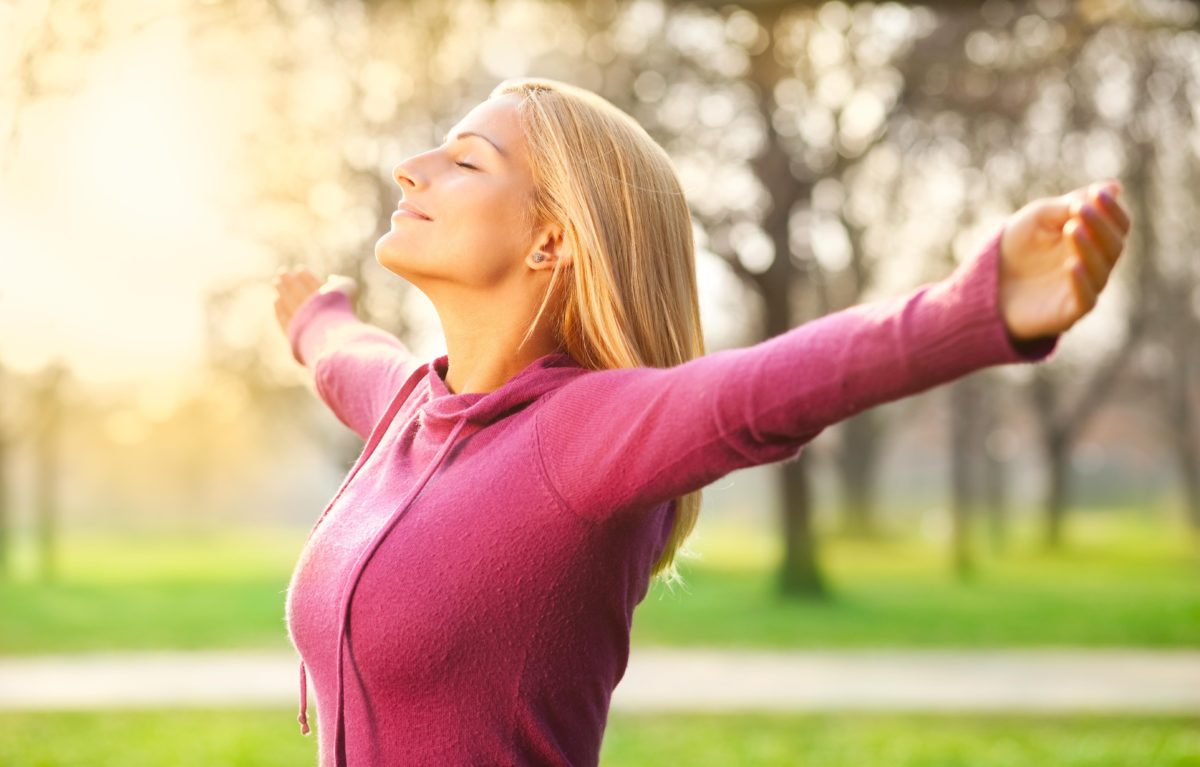 Woman standing outside with her arms out facing the sun